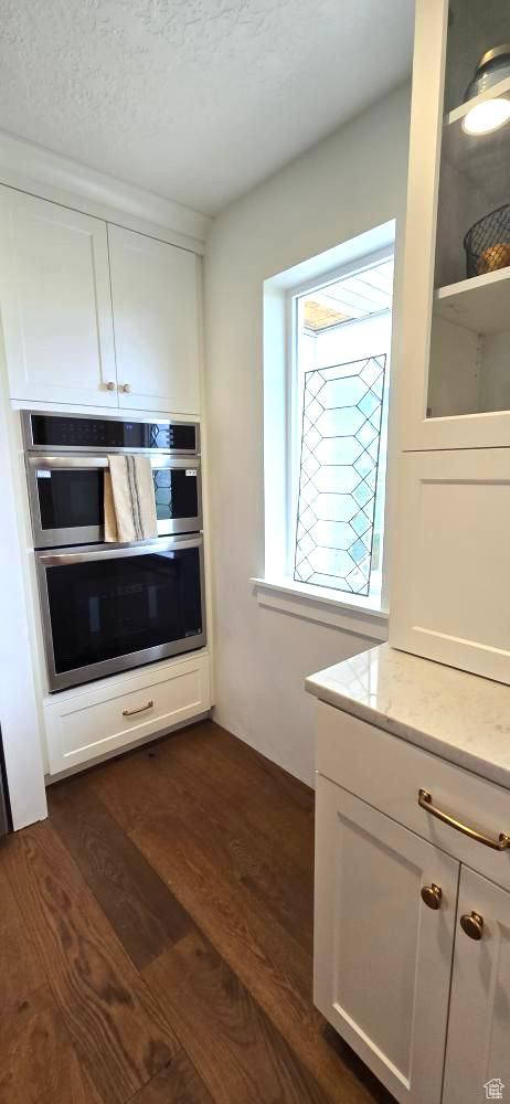kitchen featuring dark wood-style flooring, double oven, a textured ceiling, white cabinets, and light stone counters