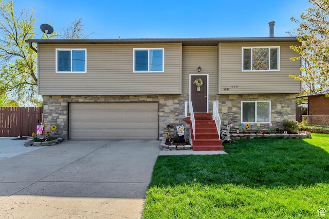 split foyer home with a front lawn, stone siding, concrete driveway, fence, and an attached garage