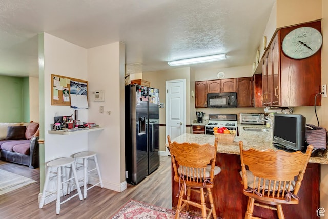 572 S Main St, Kaysville, UT 84037 - kitchen with a peninsula, light wood-style flooring, a toaster, a breakfast bar, and black appliances