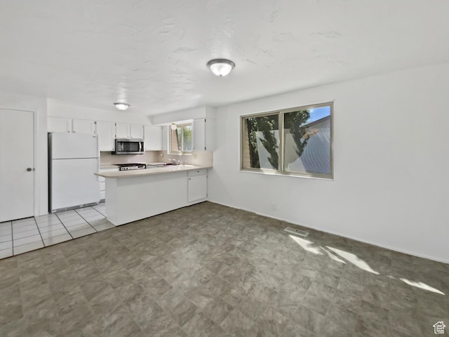 3445 W 3650 S, West Valley City, UT 84119 - kitchen featuring white cabinets, a sink, stainless steel microwave, freestanding refrigerator, and a peninsula