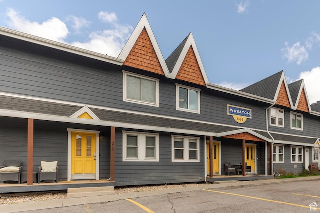 view of front of property with roof with shingles, a porch, and uncovered parking