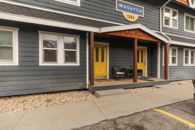 view of exterior entry with uncovered parking, a shingled roof, and covered porch