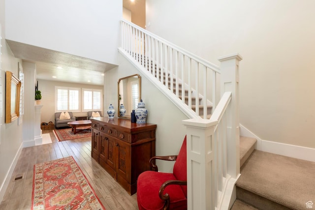 staircase featuring baseboards, wood finished floors, and a high ceiling
