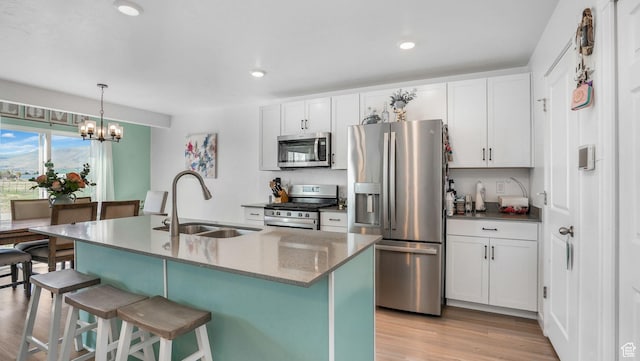 kitchen featuring a sink, an island with sink, a breakfast bar, stainless steel appliances, and light wood-style flooring