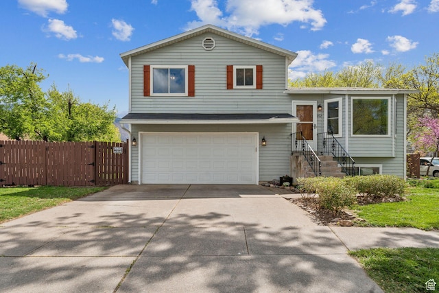 tri-level home with concrete driveway, an attached garage, and fence