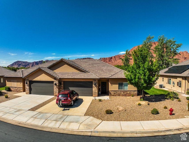 ranch-style house featuring a mountain view, driveway, stone siding, a garage, and stucco siding