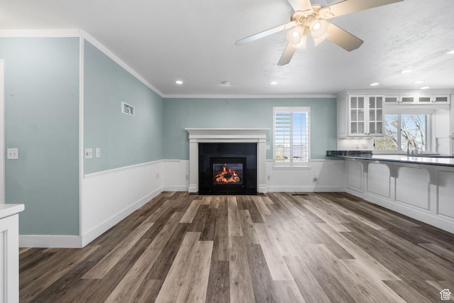 unfurnished living room featuring crown molding, a glass covered fireplace, and wood finished floors
