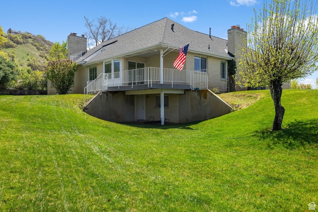 rear view of property featuring a wooden deck, a chimney, brick siding, and a yard