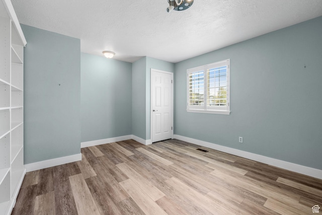 empty room with visible vents, baseboards, wood finished floors, and a textured ceiling