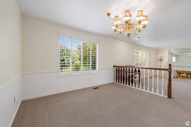 carpeted spare room featuring visible vents, baseboards, an inviting chandelier, and a high end fireplace