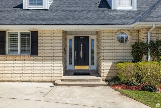 view of exterior entry featuring brick siding and a shingled roof