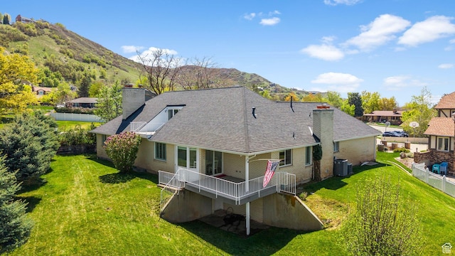 rear view of house featuring a chimney, a deck with mountain view, cooling unit, and a lawn