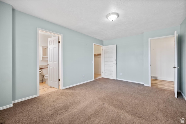 unfurnished bedroom featuring carpet flooring, a textured ceiling, ensuite bathroom, visible vents, and baseboards