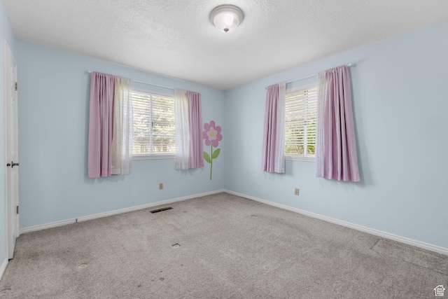 spare room featuring baseboards, visible vents, a textured ceiling, and carpet flooring