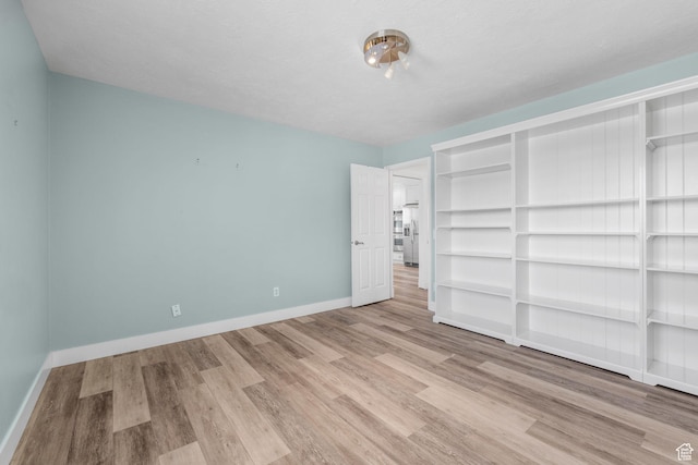 unfurnished bedroom with stainless steel refrigerator with ice dispenser, wood finished floors, and baseboards