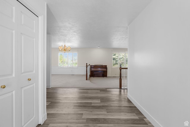 hallway featuring an inviting chandelier, wood finished floors, a textured ceiling, and baseboards