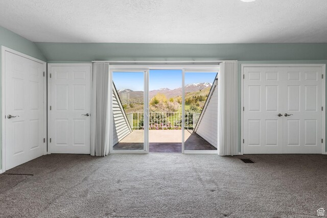 unfurnished bedroom featuring access to outside, a textured ceiling, a mountain view, and carpet