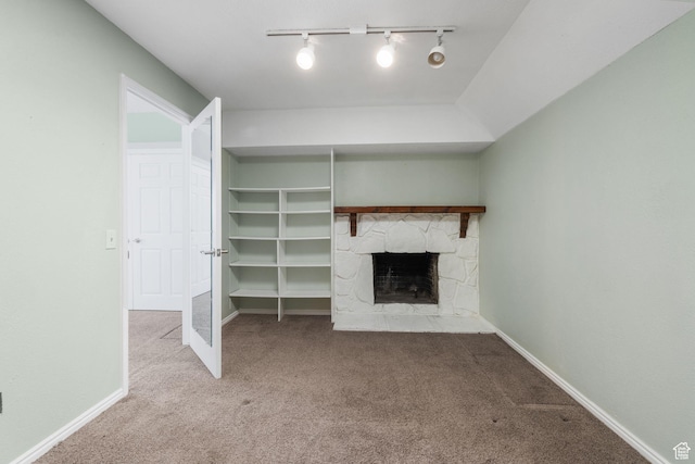 unfurnished living room with a stone fireplace, carpet, and rail lighting