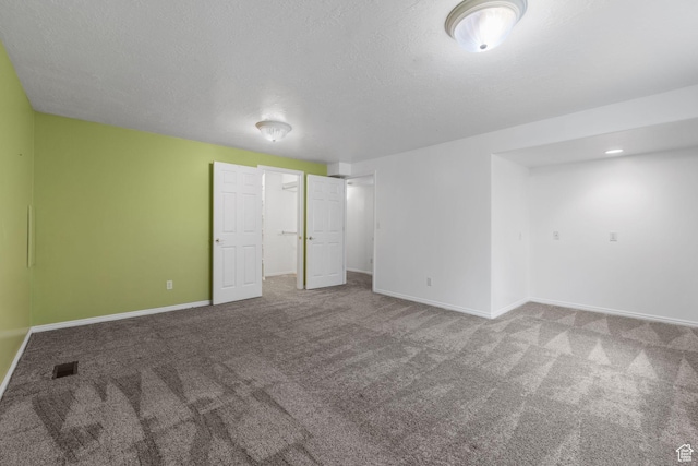 unfurnished bedroom with a textured ceiling, a walk in closet, carpet floors, baseboards, and visible vents