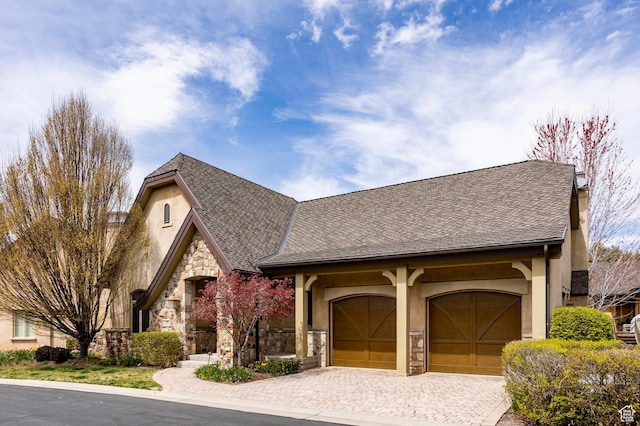 view of front of property featuring driveway, stone siding, a shingled roof, an attached garage, and stucco siding