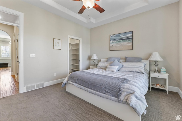 carpeted bedroom featuring a walk in closet, baseboards, a tray ceiling, and visible vents