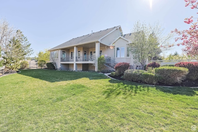 back of house featuring stucco siding, a lawn, stairway, and roof with shingles