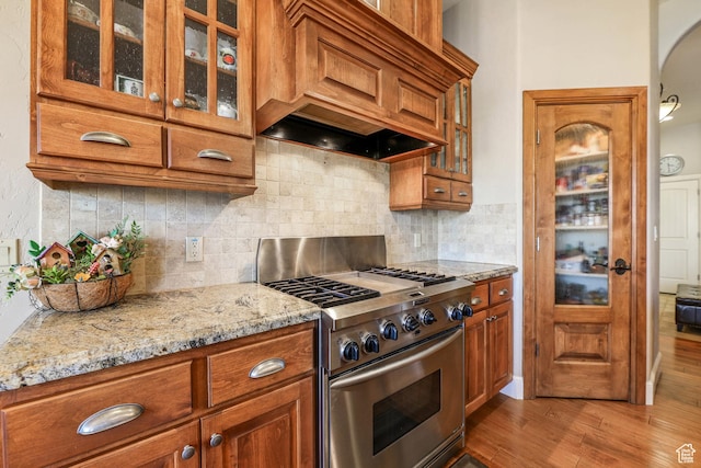 kitchen with stainless steel gas stove, brown cabinets, and custom range hood