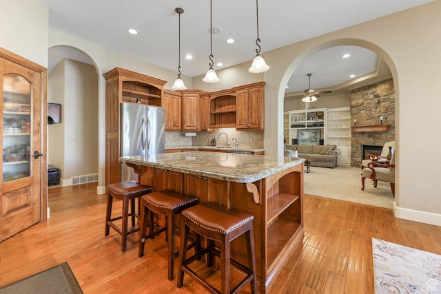 kitchen with light stone counters, open shelves, freestanding refrigerator, a fireplace, and ceiling fan