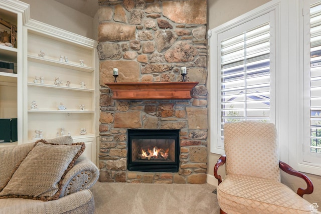carpeted living room with a stone fireplace, built in shelves, and baseboards