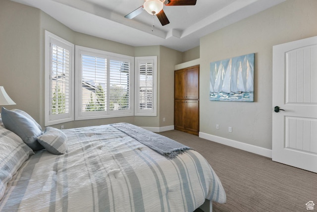 bedroom with a tray ceiling, carpet flooring, baseboards, and a ceiling fan