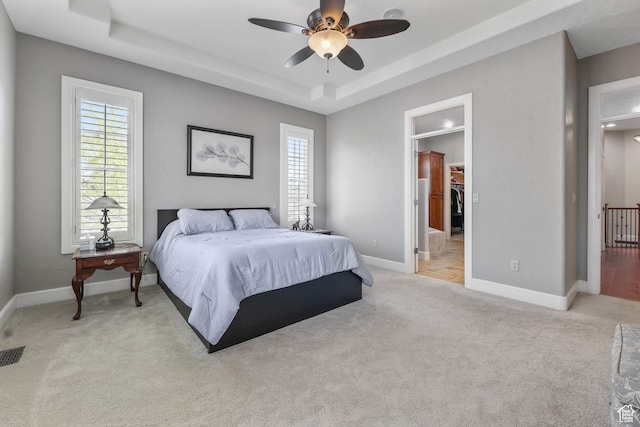 bedroom featuring light carpet, multiple windows, and a tray ceiling