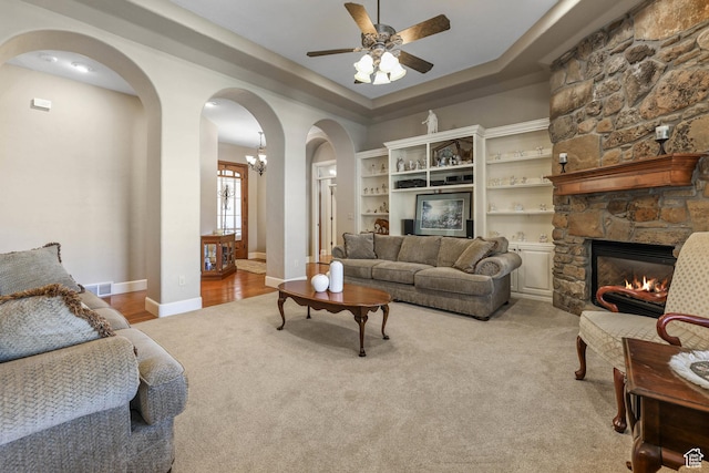 carpeted living area featuring a ceiling fan, arched walkways, a raised ceiling, a fireplace, and visible vents