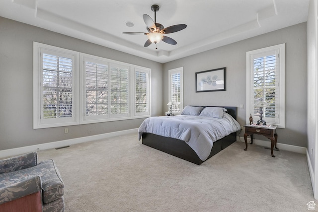 carpeted bedroom with a raised ceiling, visible vents, a ceiling fan, and baseboards
