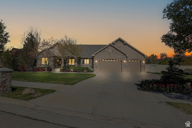 view of front of house featuring fence, concrete driveway, an attached garage, stone siding, and a lawn