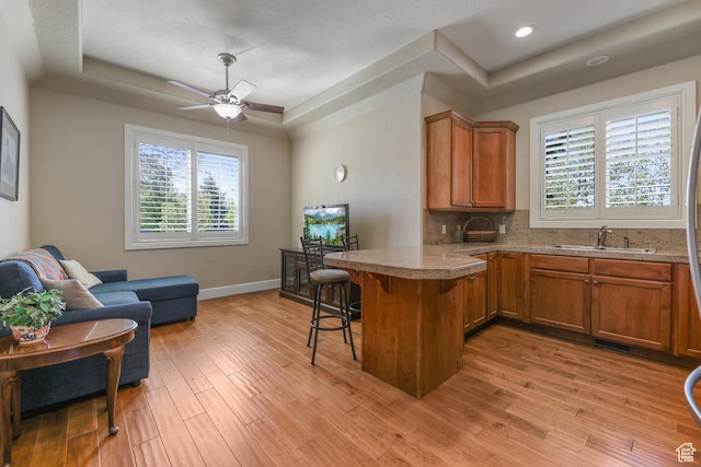 kitchen with a kitchen breakfast bar, a sink, brown cabinetry, a raised ceiling, and a peninsula