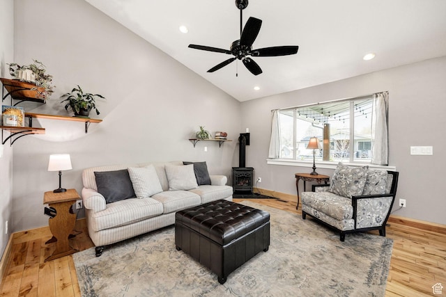 living room featuring lofted ceiling, wood finished floors, a wood stove, a ceiling fan, and baseboards