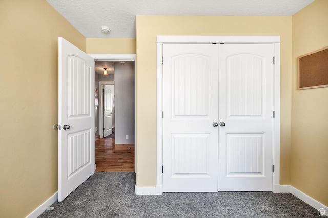 unfurnished bedroom with dark carpet, a closet, and baseboards