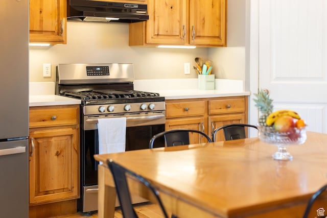 kitchen featuring light countertops, under cabinet range hood, brown cabinetry, and stainless steel appliances