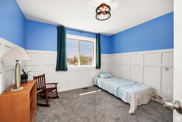 carpeted bedroom with wainscoting, a decorative wall, and visible vents