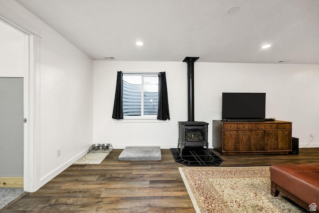living area featuring a wood stove, baseboards, dark wood-type flooring, visible vents, and recessed lighting