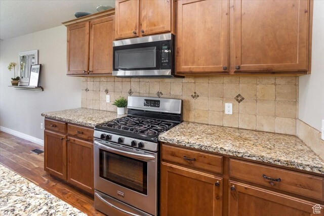 4206 Rose Springs Rd, Erda, UT 84074 - kitchen featuring stainless steel appliances, dark wood-type flooring, baseboards, brown cabinetry, and light stone counters