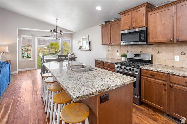 4206 Rose Springs Rd, Erda, UT 84074 - kitchen featuring stainless steel appliances, a sink, vaulted ceiling, brown cabinets, and backsplash
