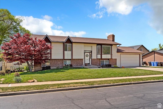 split foyer home featuring an attached garage, a chimney, brick siding, and a front yard