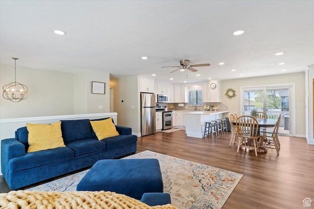 living room featuring ceiling fan with notable chandelier, baseboards, recessed lighting, and dark wood finished floors