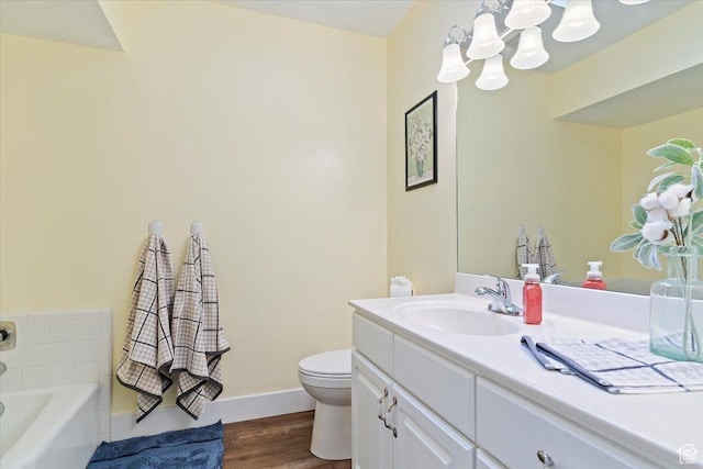 full bathroom with an inviting chandelier, wood finished floors, toilet, vanity, and a bathtub
