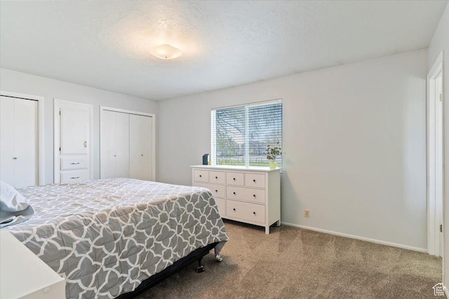 bedroom with two closets, carpet floors, a textured ceiling, and baseboards