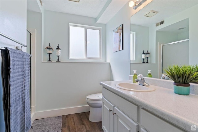 bathroom featuring wood finished floors, visible vents, toilet, vanity, and a stall shower