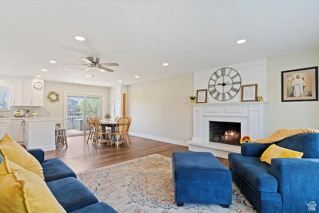 living area featuring wood finished floors, recessed lighting, a warm lit fireplace, and ceiling fan