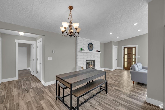 living area with wood finished floors, a textured ceiling, baseboards, a brick fireplace, and recessed lighting