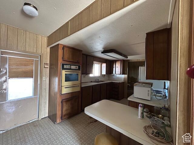 kitchen featuring wall oven, a warming drawer, wooden walls, light floors, and light countertops